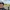 Eine Person mit Fahrradhelm macht ein Selfie auf einem betonierten Weg in ländlicher Umgebung. Hinter der Person steht ein Fahrrad. Links und rechts des Weges blühen gelbe Felder, darüber ein wolkiger Himmel.